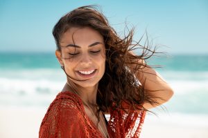 woman smiling with her hands in her hair on the beach. She goes to grief counseling in Bradenton, FL at Forever Free Counseling 34203